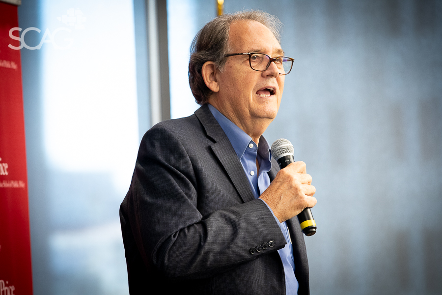 Man speaking into a microphone in a bright room.