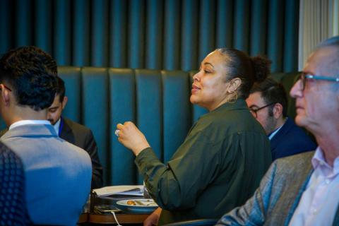 A group of people in a meeting room, one person focused and speaking.