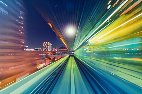 Cityscape at night with colorful light streaks, implying motion.